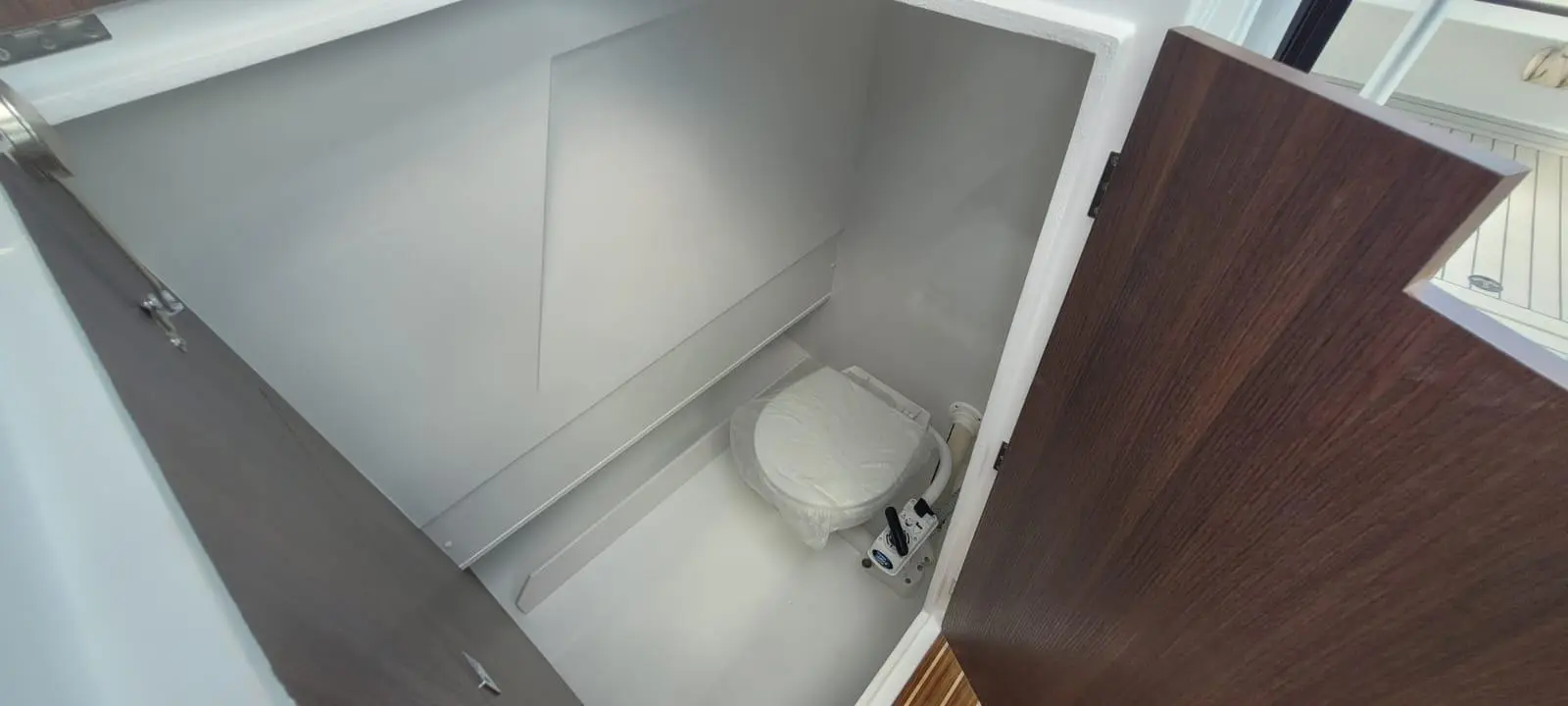 Compact boat toilet area with a white toilet, wooden door partially open, and minimalistic grey interior walls.